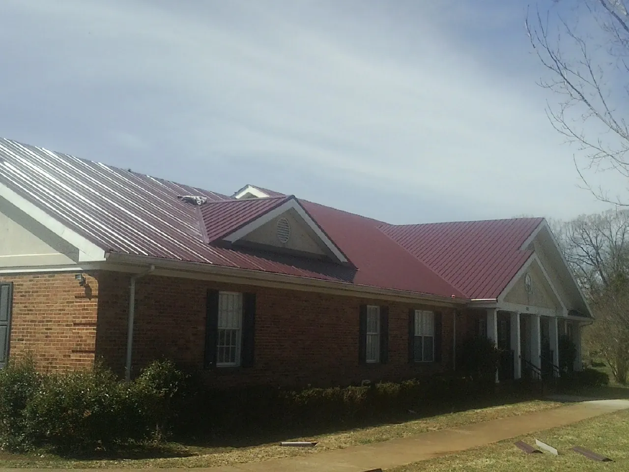 Red metal roof with gabled entries on a long brick building, from a Hail Damage Roof Repair job in Livermore