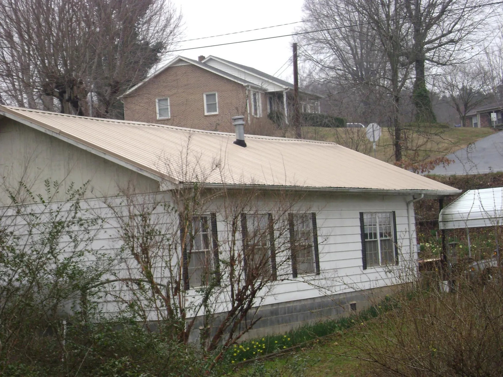 Tan metal roof on a white sided house set into a hillside — Commercial Roofing by Roofing Brothers in Livermore